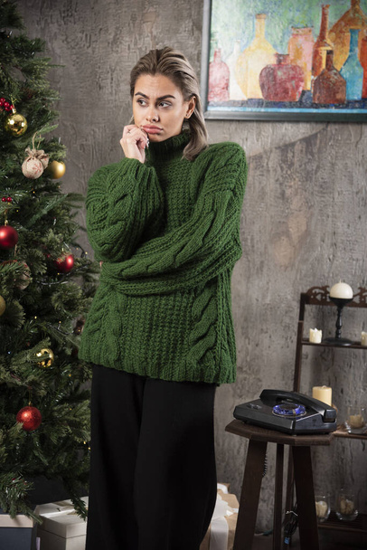 Νεαρή γυναίκα με πράσινο πουλόβερ κοιτάζει αλλού και ποζάρει. Υψηλής ποιότητας φωτογραφία - Φωτογραφία, εικόνα