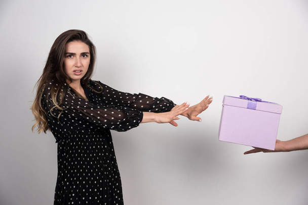 Mujer joven extiende las manos a una caja de regalo púrpura sobre un fondo blanco. Foto de alta calidad - Foto, Imagen