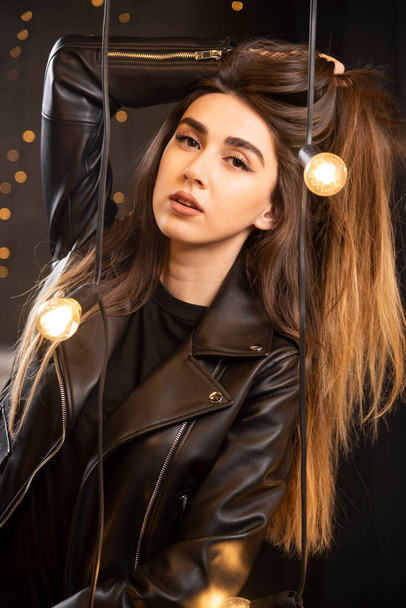 Portré egy gyönyörű fiatal modell fekete bőrdzsekiben pózol lámpák közelében. Kiváló minőségű fénykép - Fotó, kép