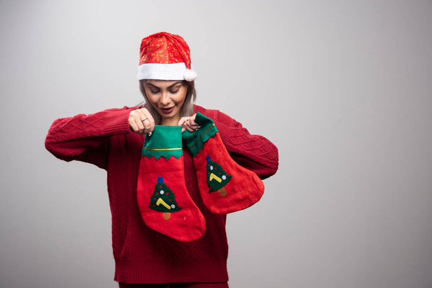 Γυναίκα με κόκκινη στολή που κοιτάζει μέσα στις χριστουγεννιάτικες κάλτσες. Υψηλής ποιότητας φωτογραφία - Φωτογραφία, εικόνα