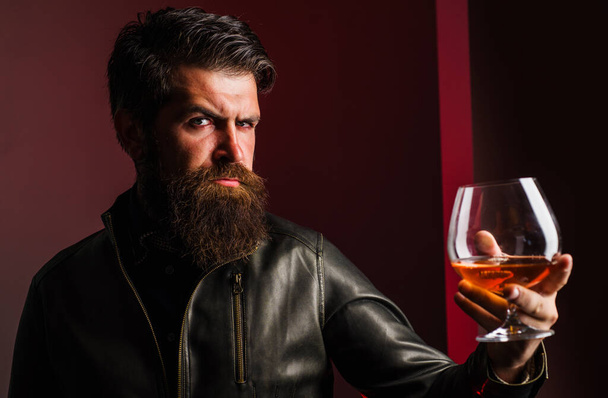 Duur drankje. Man in leren jasje drinkt cognac of cognac. Man met baard en glas whisky.. - Foto, afbeelding
