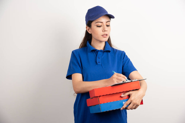 Woman courier writing in clipboard and holding cardboards of pizza - Fotoğraf, Görsel