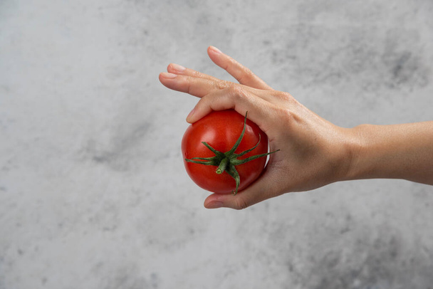 Ręka trzymająca świeży czerwony pomidor na marmurowym tle. Wysokiej jakości zdjęcie - Zdjęcie, obraz