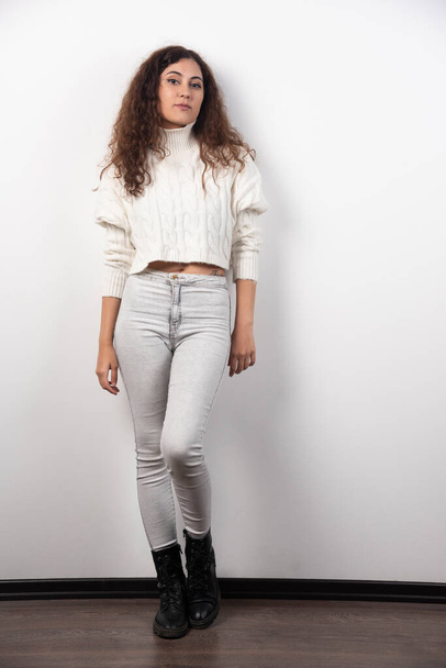 Young woman in white sweater standing over a white wall. High quality photo - Foto, afbeelding