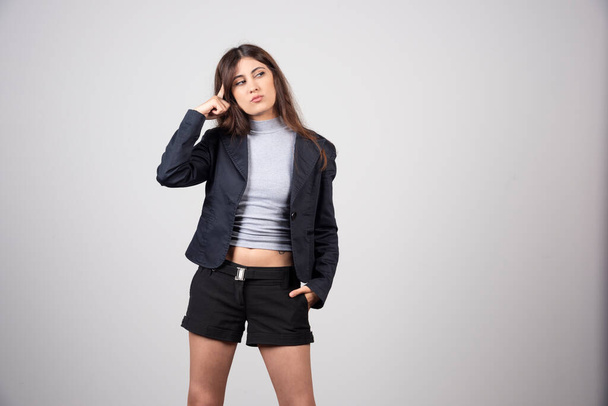 Jovem mulher de negócios de jaqueta em pé e posando sobre uma parede cinza. Foto de alta qualidade - Foto, Imagem