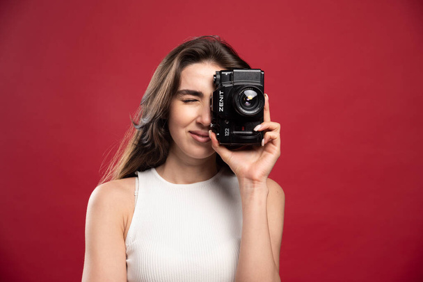 Kaunis nainen ottaa kuvia, joissa on kamera punaisella taustalla. Laadukas kuva - Valokuva, kuva