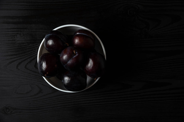 Black plums in a white ceramic saucer. High quality photo - Foto, Bild