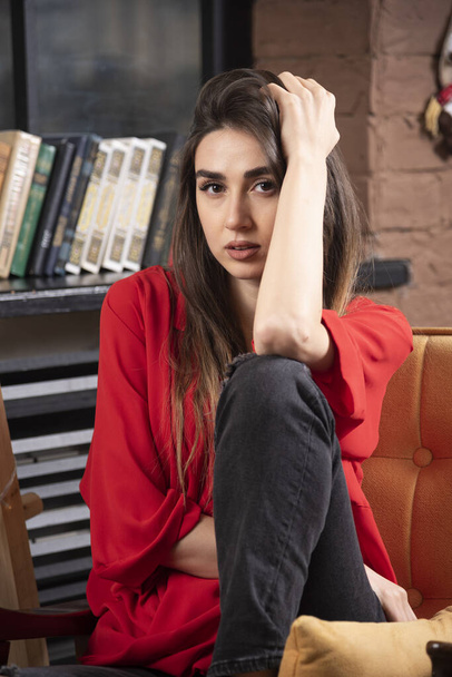 Una joven modelo en blusa roja sentada y posando. Foto de alta calidad - Foto, Imagen