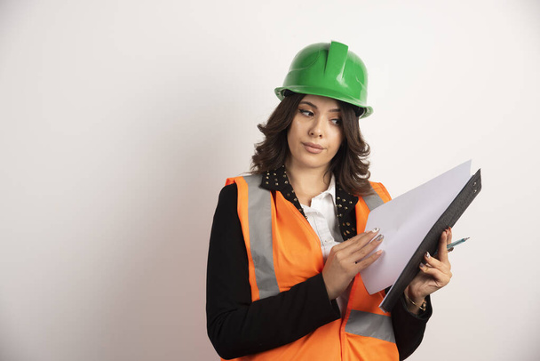 Vrouwelijke ingenieur kijkt door notitieboekje op witte achtergrond. Hoge kwaliteit foto - Foto, afbeelding