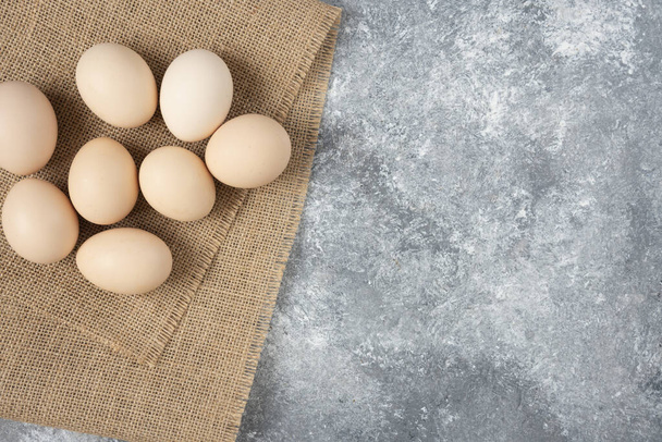 Raw organic eggs placed on top of sackcloth on marble background. High quality photo - Фото, зображення
