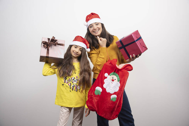 Két fiatal lány karácsonyi ajándékokkal egy fehér fal fölött. Kiváló minőségű fénykép - Fotó, kép