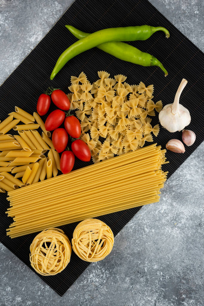 Various raw pasta and vegetables on black bamboo sheet. High quality photo - Photo, Image