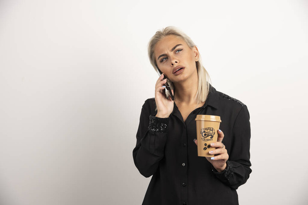 Nainen puhuu kännykällä ja pitelee kahvikuppia. Laadukas kuva - Valokuva, kuva
