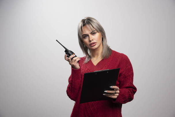 Young female with radio transceiver and clipboard posing on gray background. High quality photo - Photo, Image