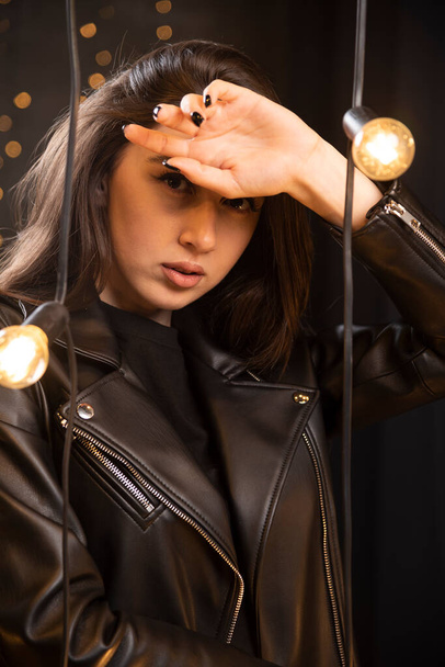 Portret pięknej młodej modelki w czarnej skórzanej kurtce, pozującej przy lampach. Wysokiej jakości zdjęcie - Zdjęcie, obraz