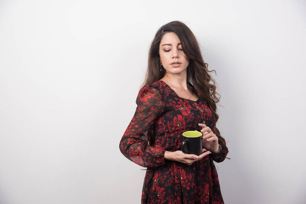 Faliste włosy kobieta z filiżanką herbaty stojącej na szarym tle. Wysokiej jakości zdjęcie - Zdjęcie, obraz