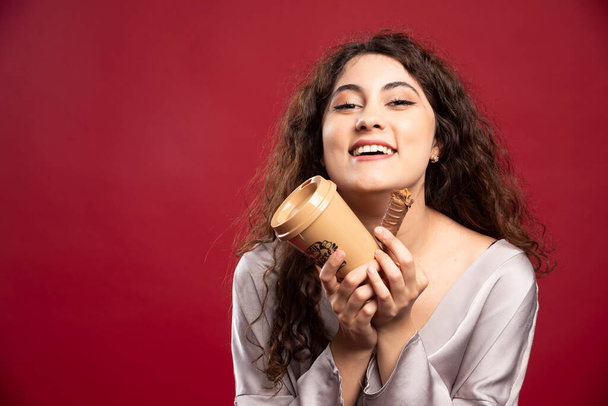Šťastná žena drží kávu a čokoládu na červeném pozadí. Kvalitní fotografie - Fotografie, Obrázek