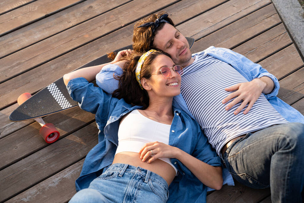 Despreocupado jovem casal deitado no skate abraçando desfrutar do pôr do sol juntos. Relação e estilo de vida - Foto, Imagem