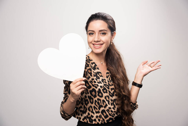 Businesswoman in leopard printed shirt holding a heart shape blank board. High quality photo - Foto, immagini