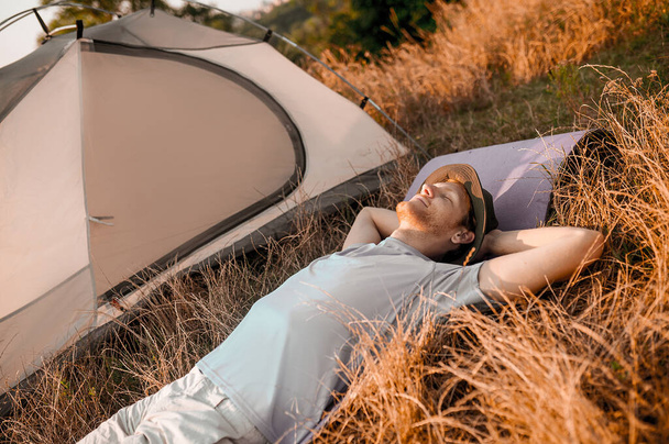 Ein Mann liegt auf dem Gras neben seinem Zelt und schläft - Foto, Bild