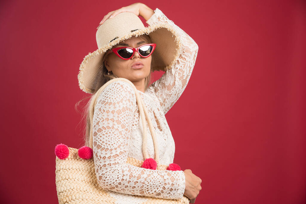Pretty woman walking with bag and hat on red background. High quality photo - Φωτογραφία, εικόνα