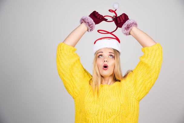 Beautiful girl in a yellow sweater looking at Santa's hat . High quality photo - Photo, Image