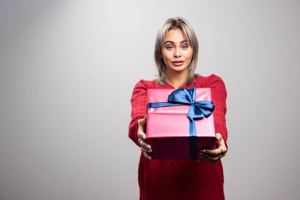Young woman in red sweater offering Christmas gift. High quality photo - Φωτογραφία, εικόνα