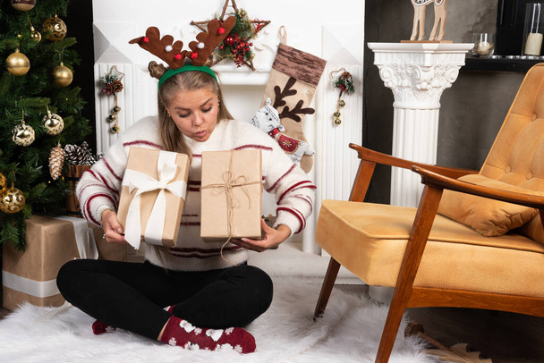 Молодая женщина в оленьих ушах смотрит на два рождественских подарка. Высокое качество фото - Фото, изображение