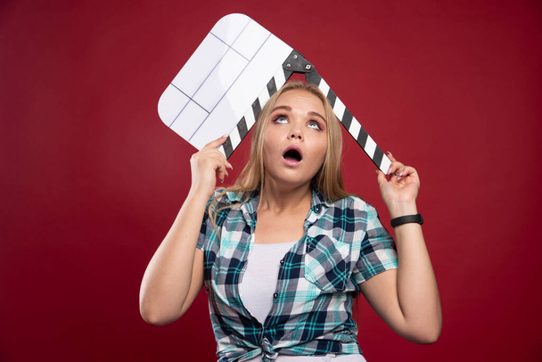 Young blonde model holding a blank movie filming clapper board and looks stressed and unexperienced. High quality photo - Photo, Image