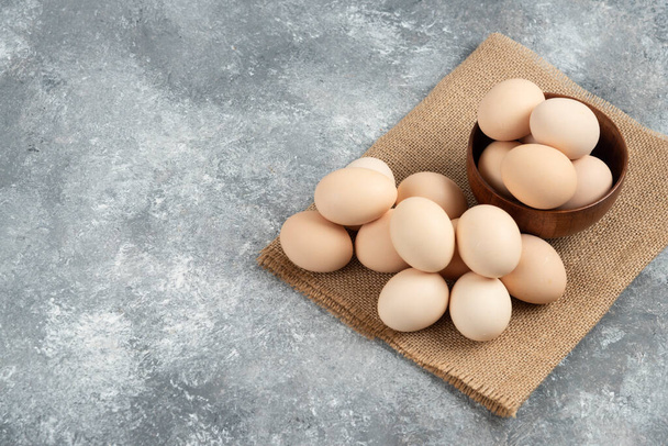 Puinen kulho orgaanisia raakoja munia marmoripinnalla. Laadukas kuva - Valokuva, kuva