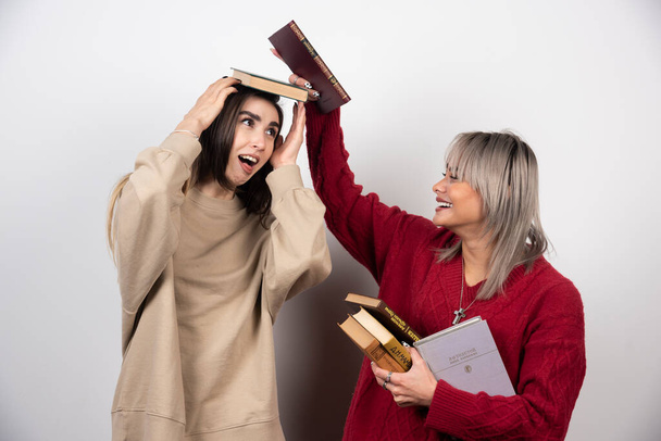 Girl in red sweater hitting another girl with book. High quality photo - Photo, image