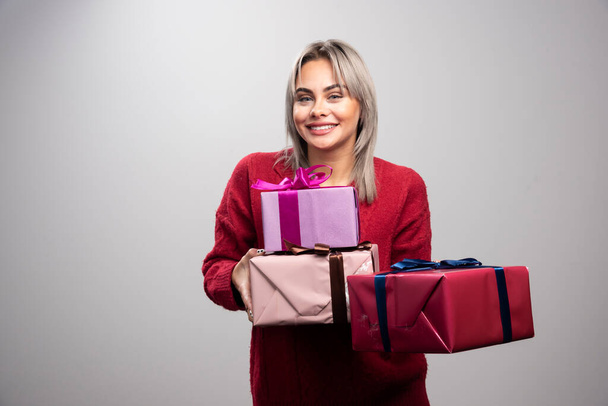 Porträt einer fröhlichen Frau, die Weihnachtsgeschenke auf grauem Hintergrund anbietet. Hochwertiges Foto - Foto, Bild