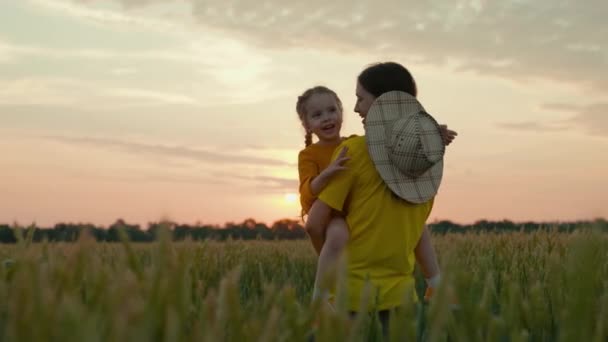 Μητέρα αγρότισσα με ένα μικρό παιδί στην αγκαλιά της περπατά στο χωράφι με σιτάρι, ευτυχισμένη οικογένεια, αγρονόμος γυναίκα, επιχειρηματική γεωργία, καλλιέργεια καλλιεργειών στην ύπαιθρο, ωρίμανση στο έδαφος - Πλάνα, βίντεο
