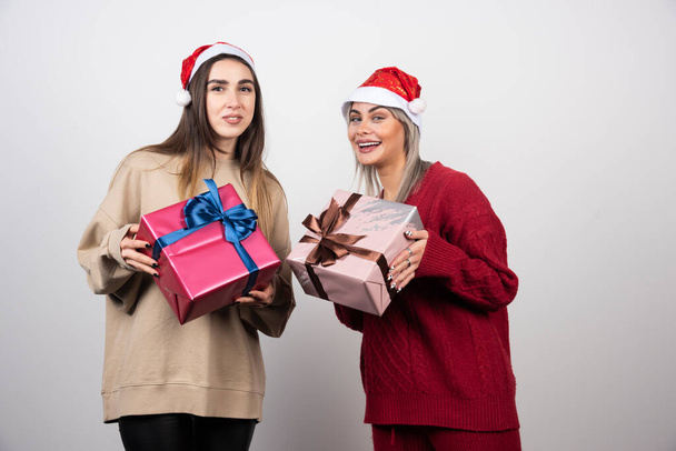 Dos chicas sonrientes en Santa Sombrero sosteniendo regalos festivos de Navidad. Foto de alta calidad - Foto, imagen