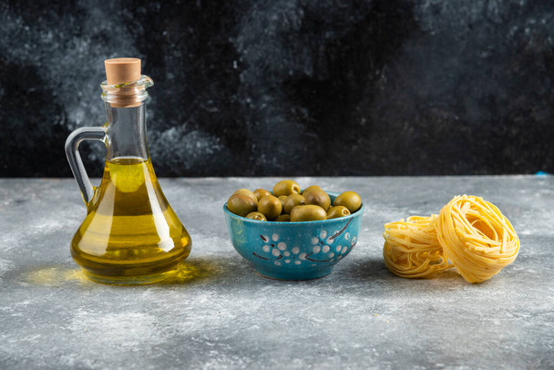 Nuudeleita, öljyä ja vihreitä oliiveja kivipöydällä. Laadukas kuva - Valokuva, kuva