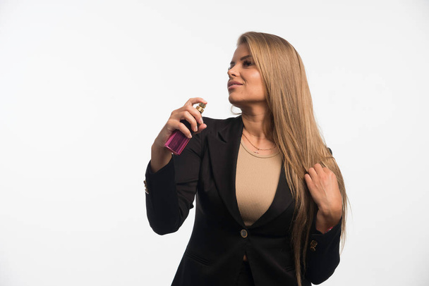 La joven empresaria con traje negro se aplica perfume en el cuello. Foto de alta calidad - Foto, Imagen