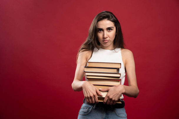 Female student carrying lots of books on a red background. High quality photo - Foto, Imagen
