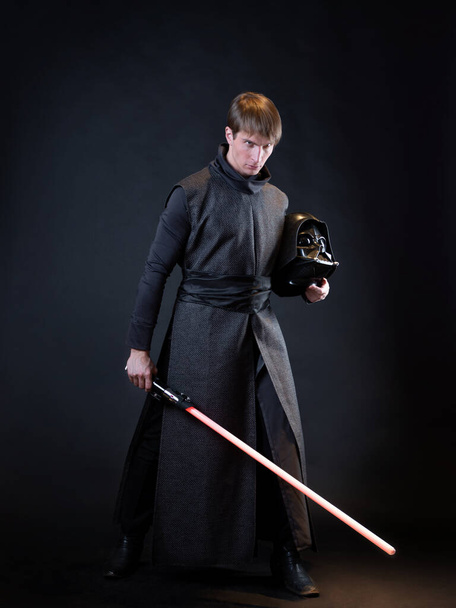 A villain with a red lightsaber, a young man in a long robe does fighting poses, - Фото, изображение