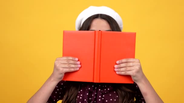 smart schoolgirl in glasses hiding behind hard cover notebook for reading and studying, literature - Footage, Video