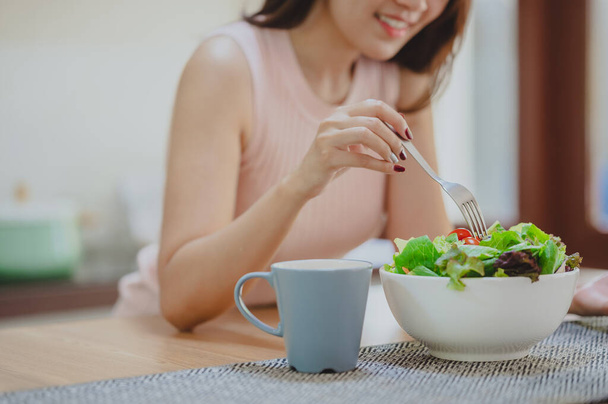 Cropped shot of happy woman eating fresh vegetable salad in white bowl in kitchen.  enjoying a healthy food - Фото, изображение