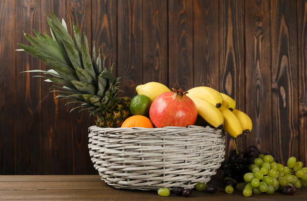 Wicker bowl with different ripe fruits on wooden table - Fotografie, Obrázek