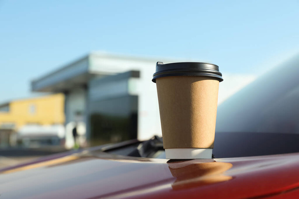 Paper coffee cup on car hood near gas station. Space for text - Foto, afbeelding