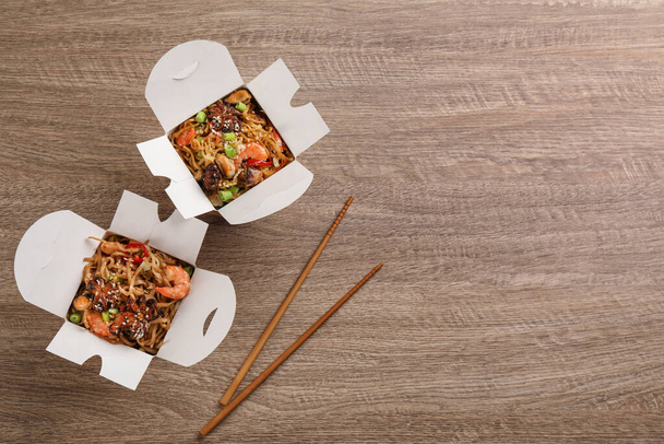 Boxes of wok noodles with seafood and chopsticks on wooden table, flat lay. Space for text - Фото, зображення