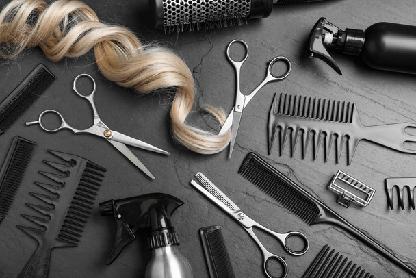 Flat lay composition of professional scissors, hair strand and other hairdresser's equipment on black table. Haircut tool - Foto, Imagem