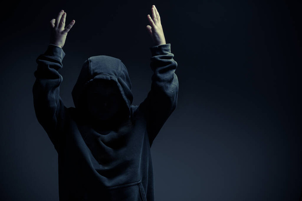 Um retrato de uma criança com capuz, levantando as mãos, no ambiente escuro - Foto, Imagem
