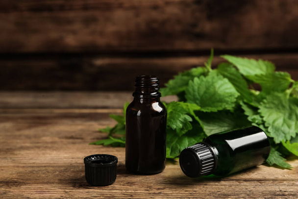 Glass bottles of nettle oil with leaves on wooden table - Фото, зображення