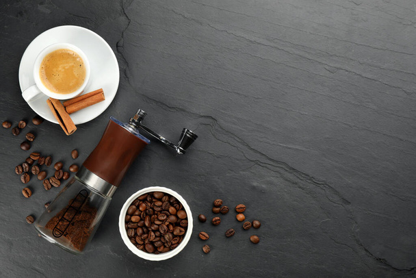 Modern manual coffee grinder with powder, beans and cup of aromatic drink on black table, flat lay. Space for text - Foto, Bild