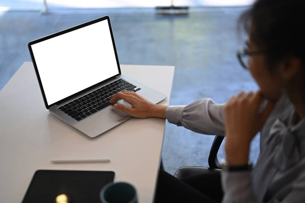 オフィスのデスクで空白の画面を持つラップトップコンピュータ上で働く若い実業家の側面図. - 写真・画像
