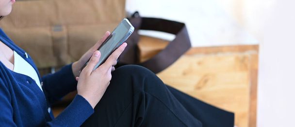 Πλευρική άποψη του νεαρού θηλυκού ελέγχου εισοδήματος μήνυμα στο κινητό τηλέφωνο, ενώ κάθεται στο πάτωμα. - Φωτογραφία, εικόνα
