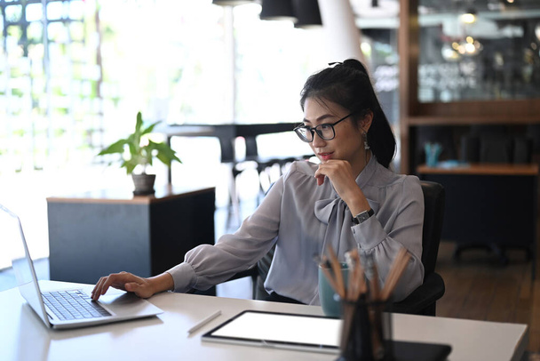 Бізнес-леді в окулярах з використанням комп'ютерного ноутбука для онлайн-програмного забезпечення для аналізу даних в офісі
. - Фото, зображення